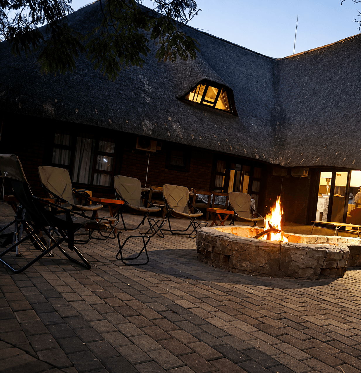 The Bougasvlei Safaris bushveld lodge glowing at dusk with a lit firepit and lounge chairs